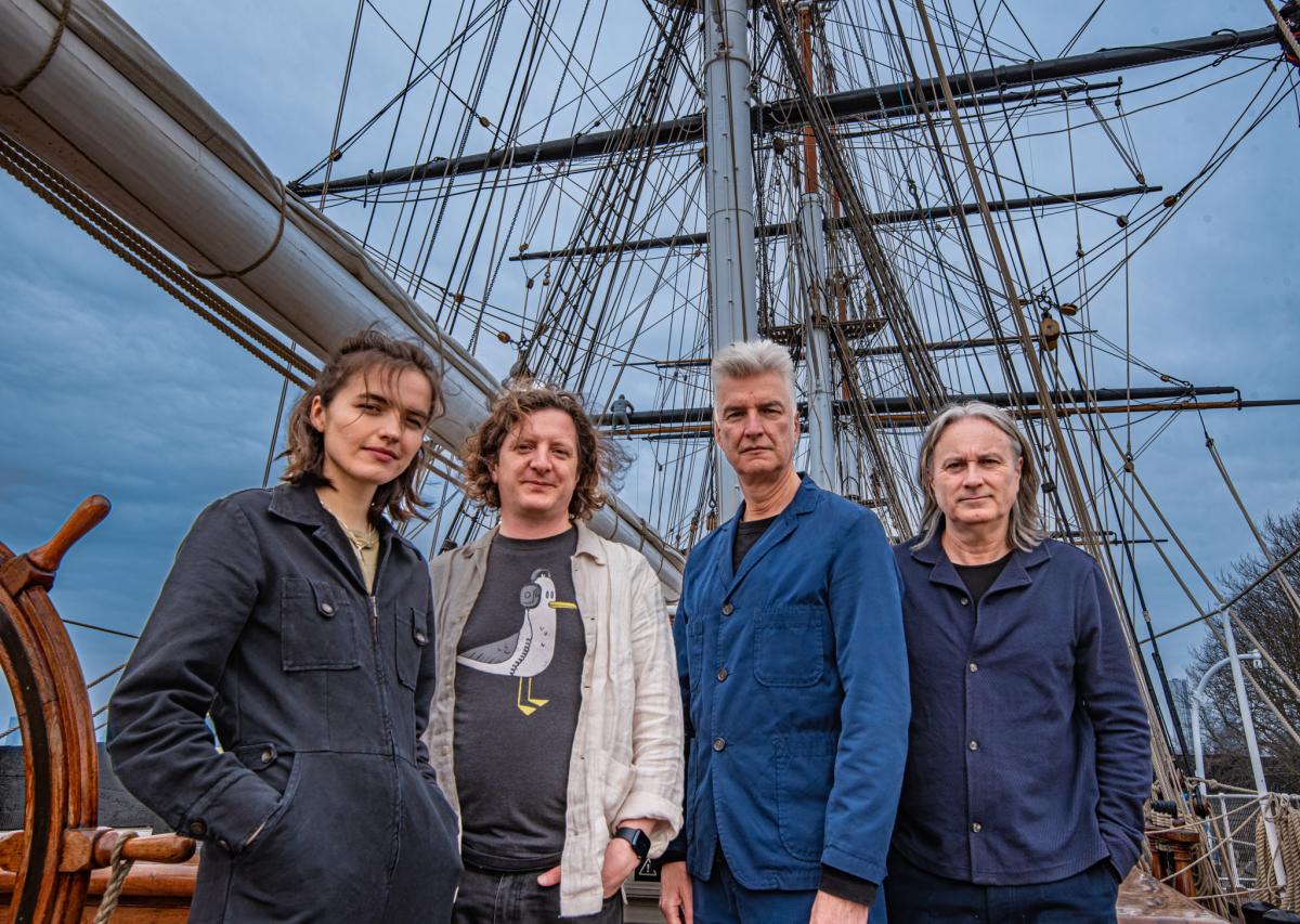 Portrait photo of the band Blue Machine, featuring the group of four stood on board historic ship Cutty Sark