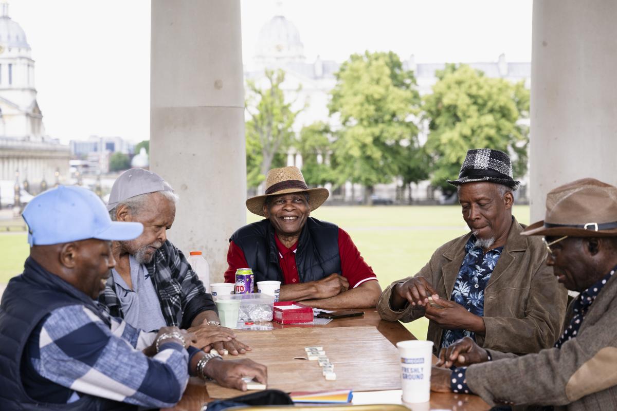 Photo of group of men sitting around a table playing a dominoes game and smiling