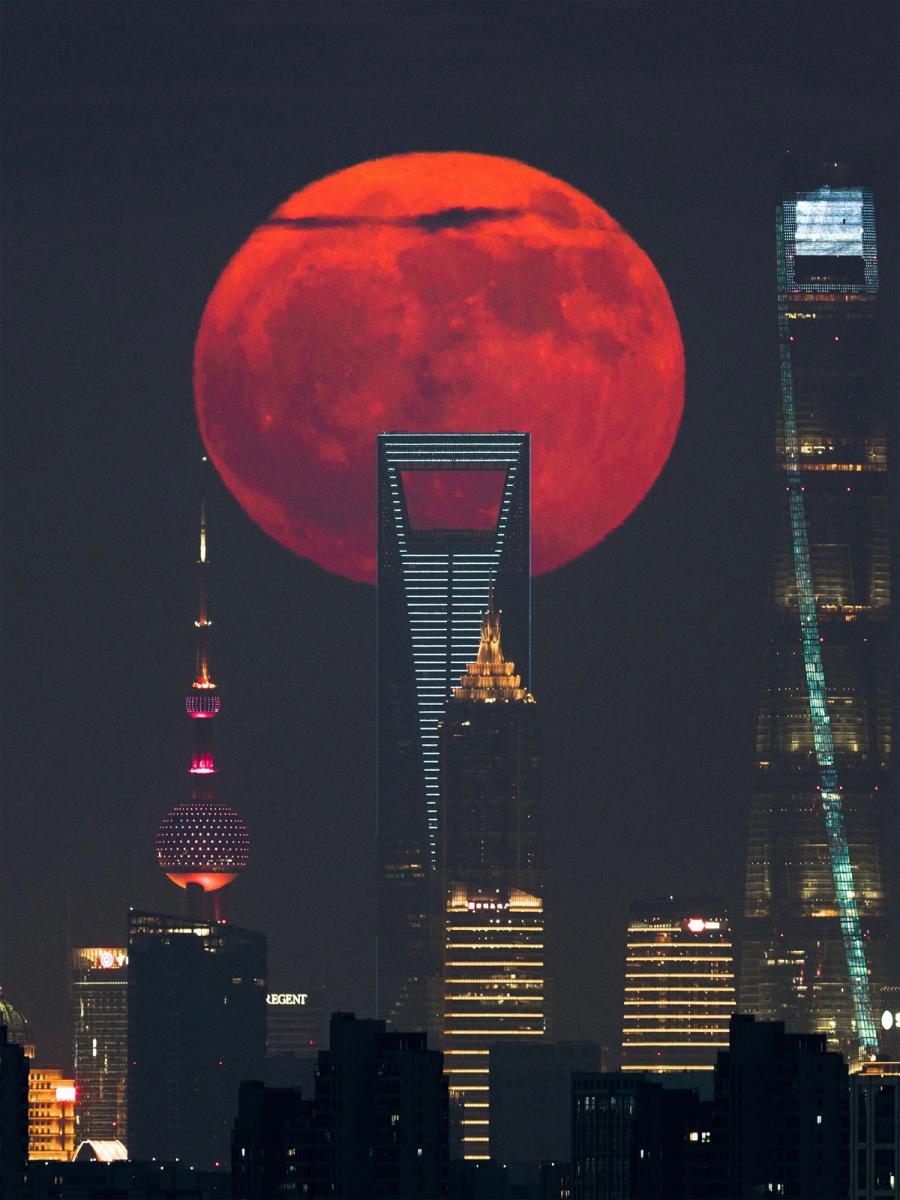 Huge blood red moon rising at night behind Shanghai skyscrapers