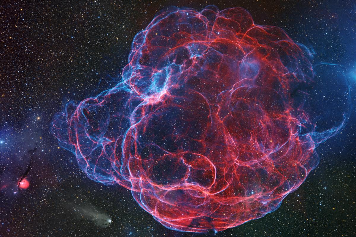 Vivid photo of a nebula in reds, purples and blues, resembling a large bubble