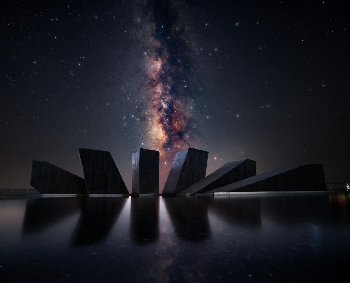 Vivid Milky Way core vertical in sky over sculpture of black stones with water in foreground