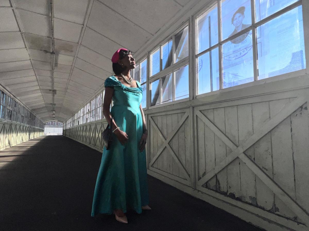 Still from Here I Stand showing woman in long green dress on Tilbury Bridge walkway