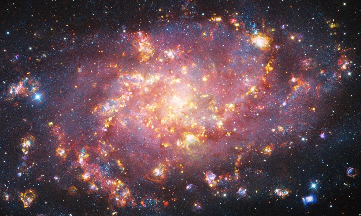 Photo of M33, the Triangulum Galaxy, resembling fireworks with bright spots of white, purple and reds against black background
