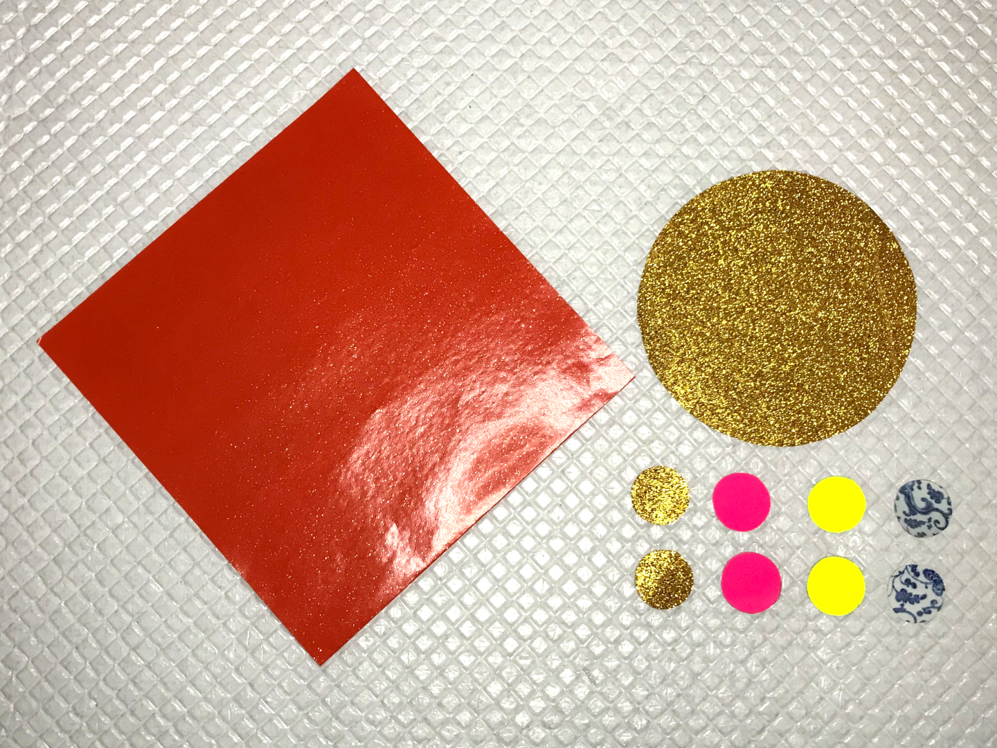 A piece of red paper in a square. A piece of gold paper in a large circle. Eight small circles in gold, pink, yellow and blue patterned paper.