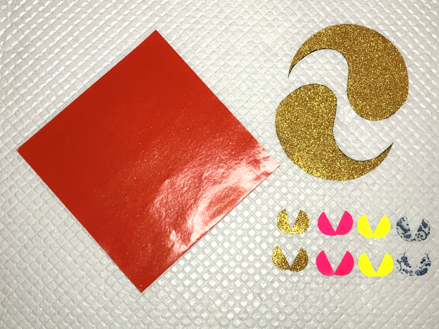 A square piece of red paper. Two pieces of gold paper cut into ying-yang shapes (or teardrops). Eight small circles cut almost in half.