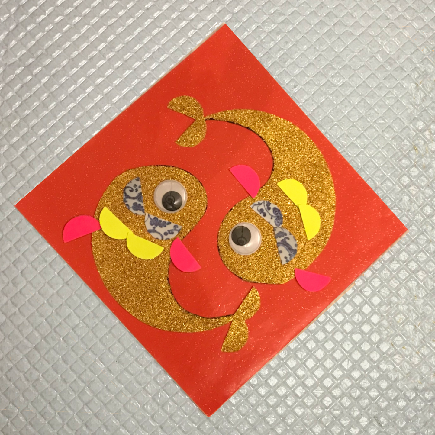 A piece of red square paper with two fish decorated on using cut out paper shapes.