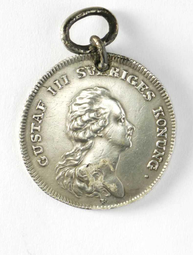 Collection image of a medal awarded for bravery at sea. Medal looks like a coin with a head in profile and a hole drilled in the top with a ring attached