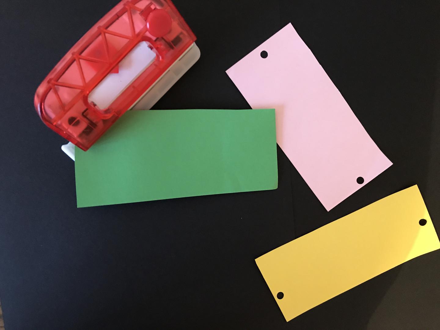 Three strips of coloured pieces of paper. Two have small holes at either end. 