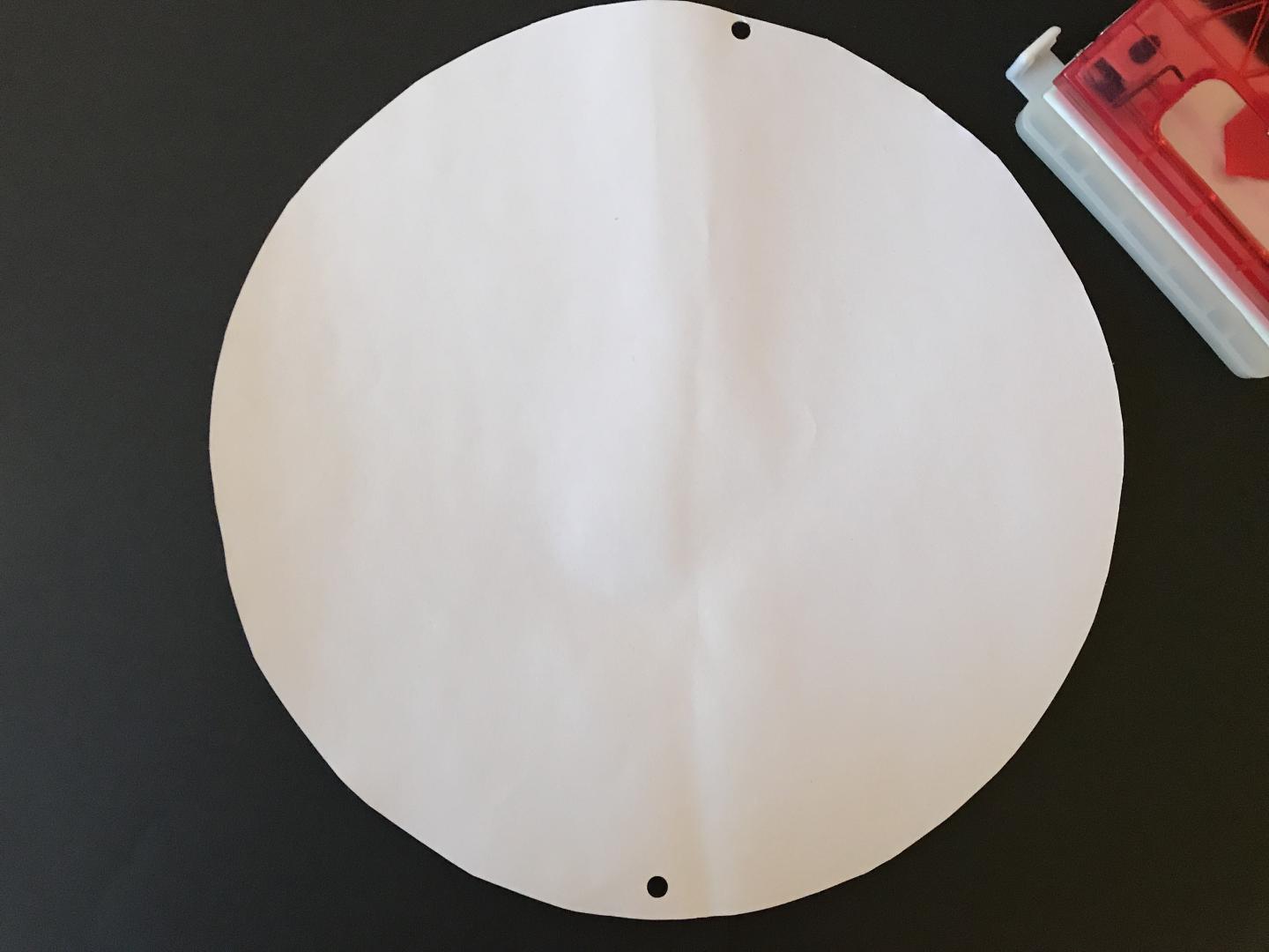 A piece of card cut into a circle. Two holes have been made opposite each other.