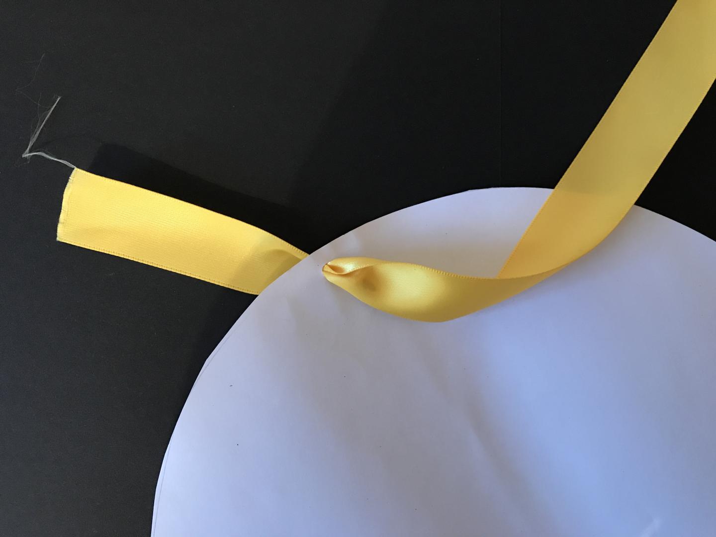 Yellow ribbon is threaded through a small hole in a paper circle.