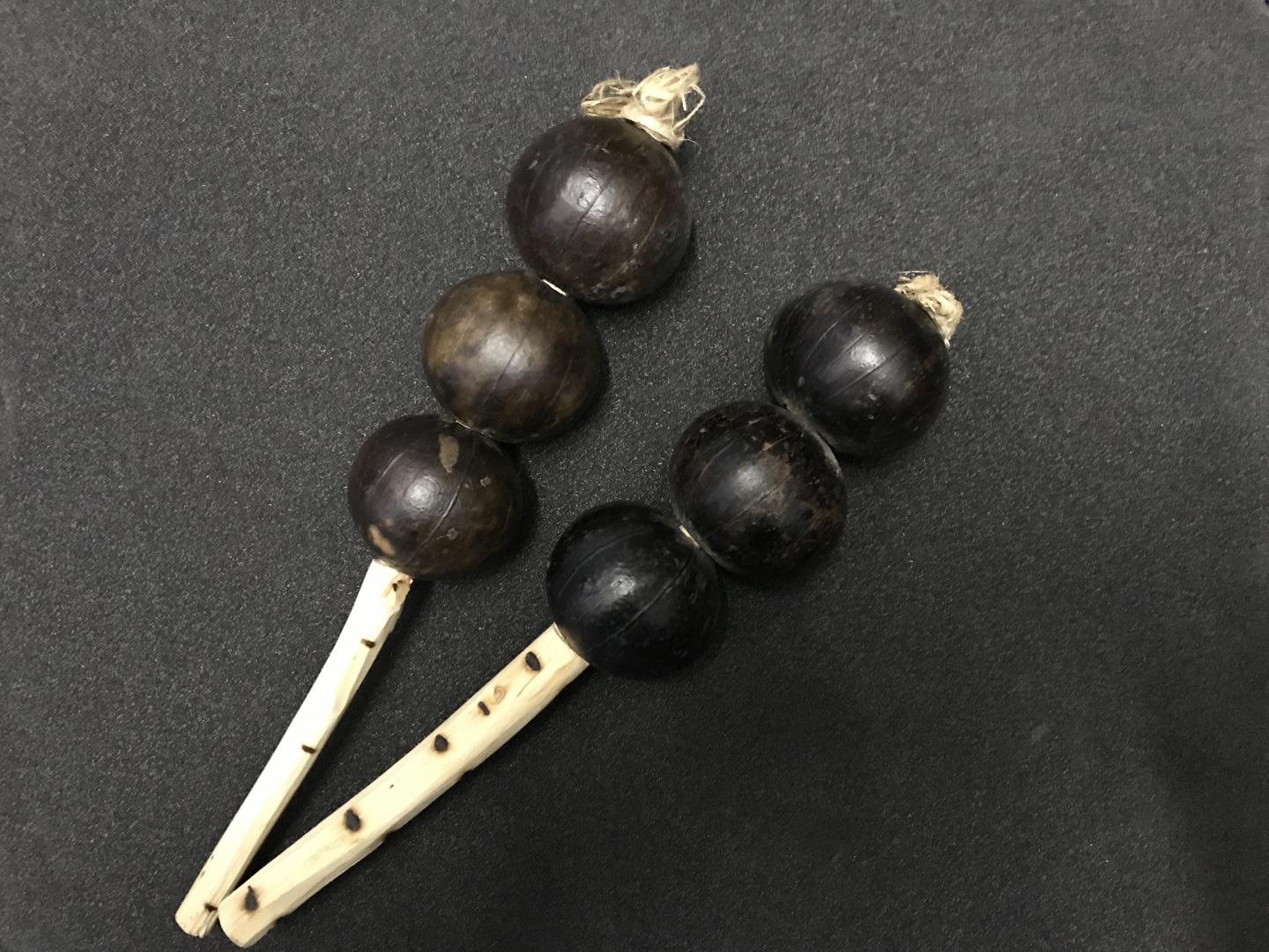 Two instruments made of three seed pods each on a stick.