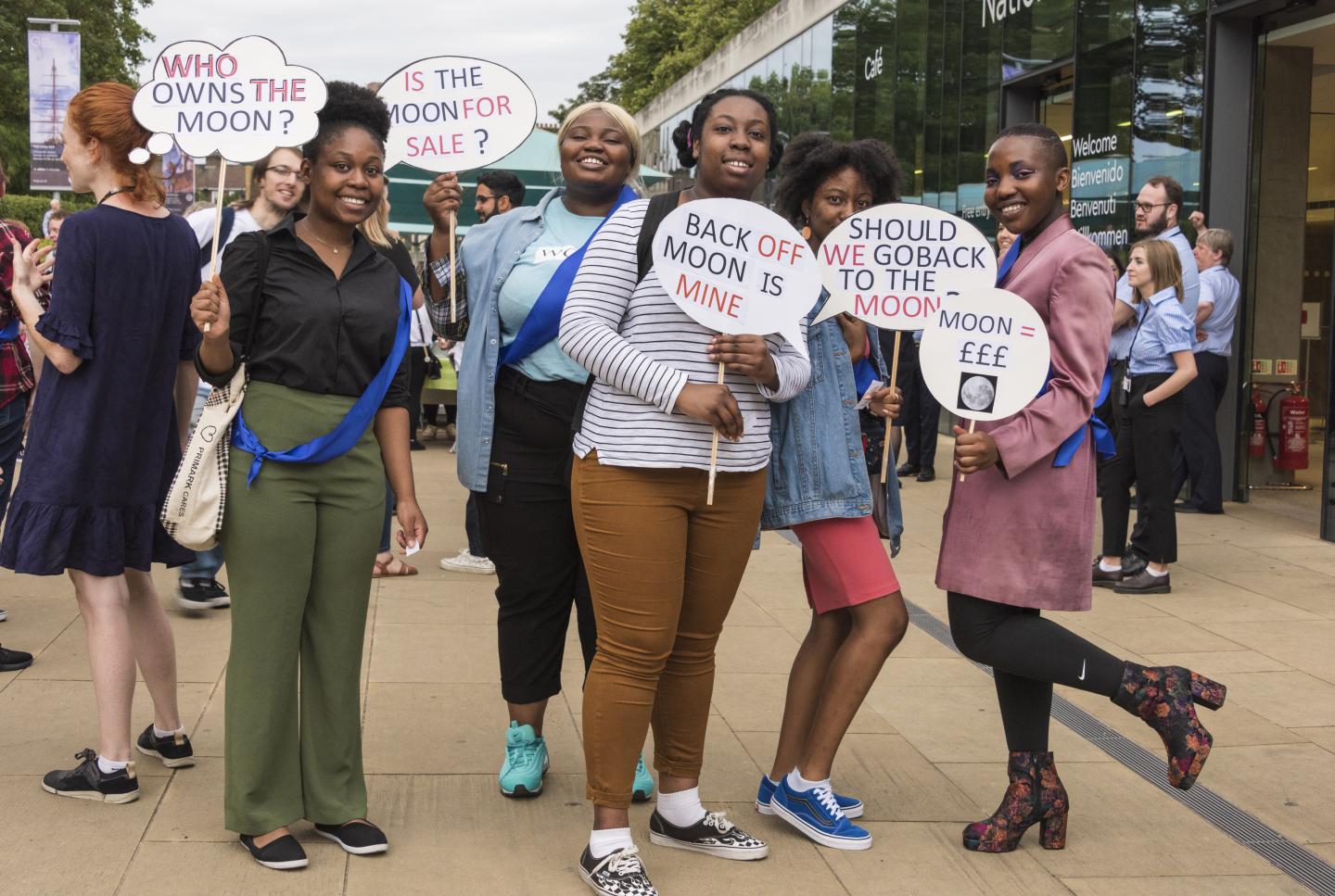 A group of young people holding placards that ask questions about the ownership of the moon