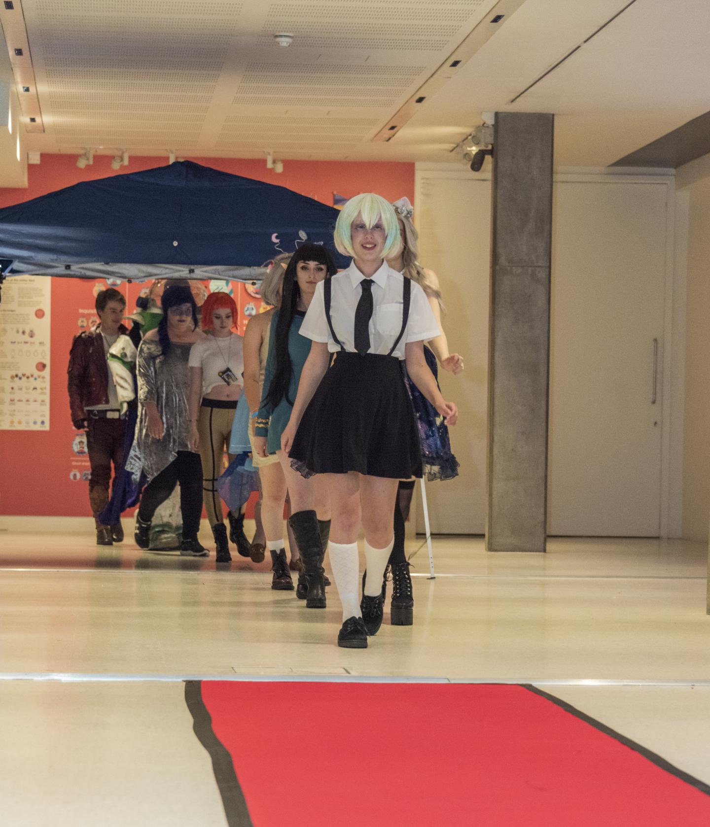 A group of young people in a line in costume walk a red carpet