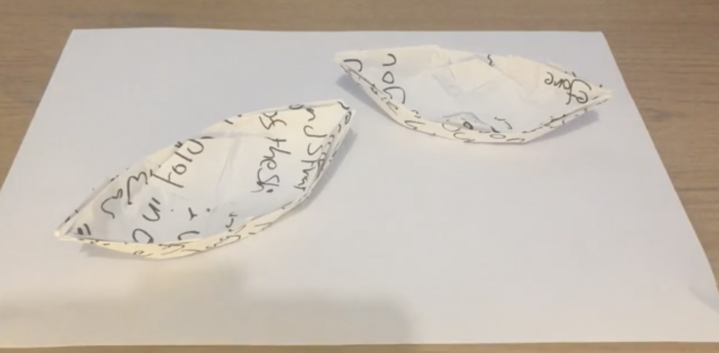 2 ships folded out of paper using origami. There is some illegible writing on the paper.