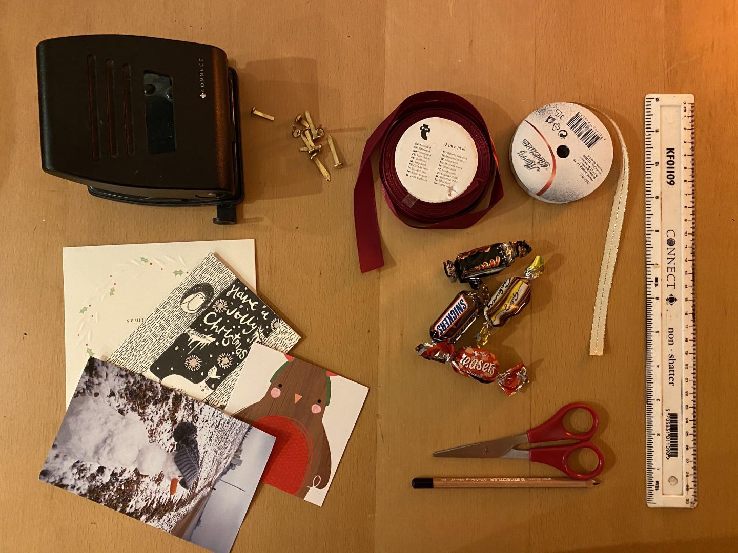 table with Scissors, split pins, ribbon, old christmas cards, chocolates, pencil, ruler, hole punch