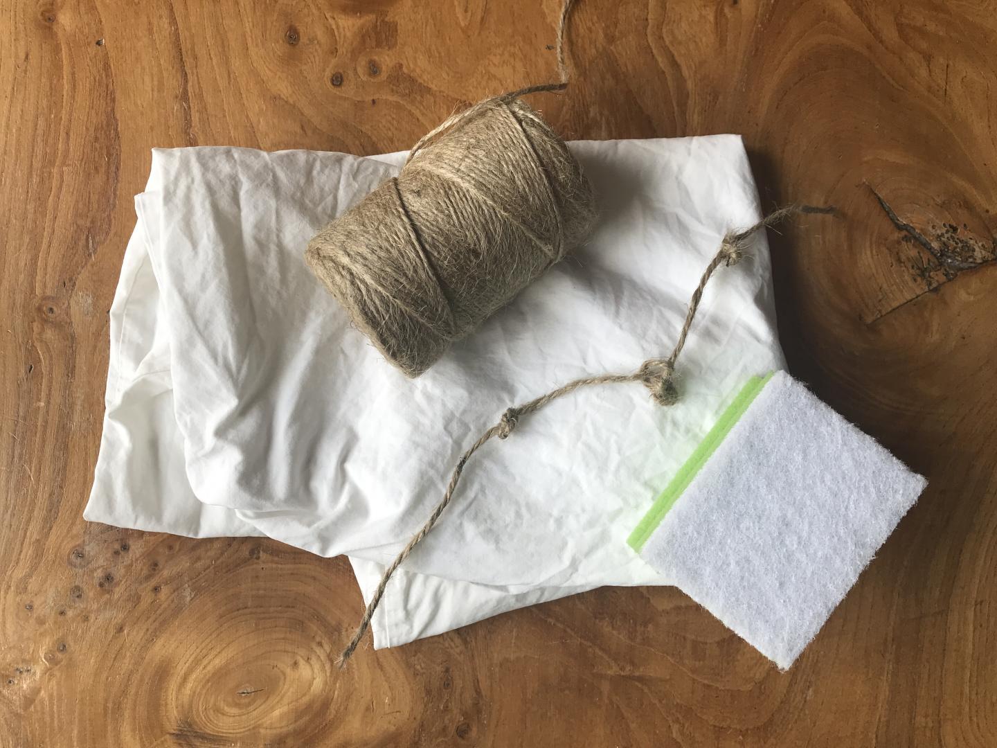 A pillowcase with a roll of string, sponge and piece of string with knots tied into it.