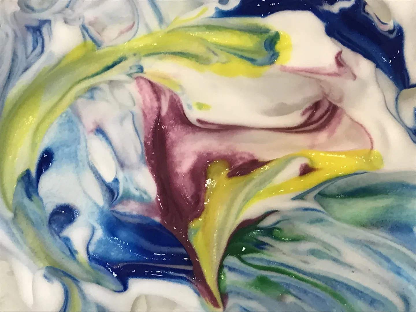 Purple, blue, green and yellow paint is mixed into shaving foam. 