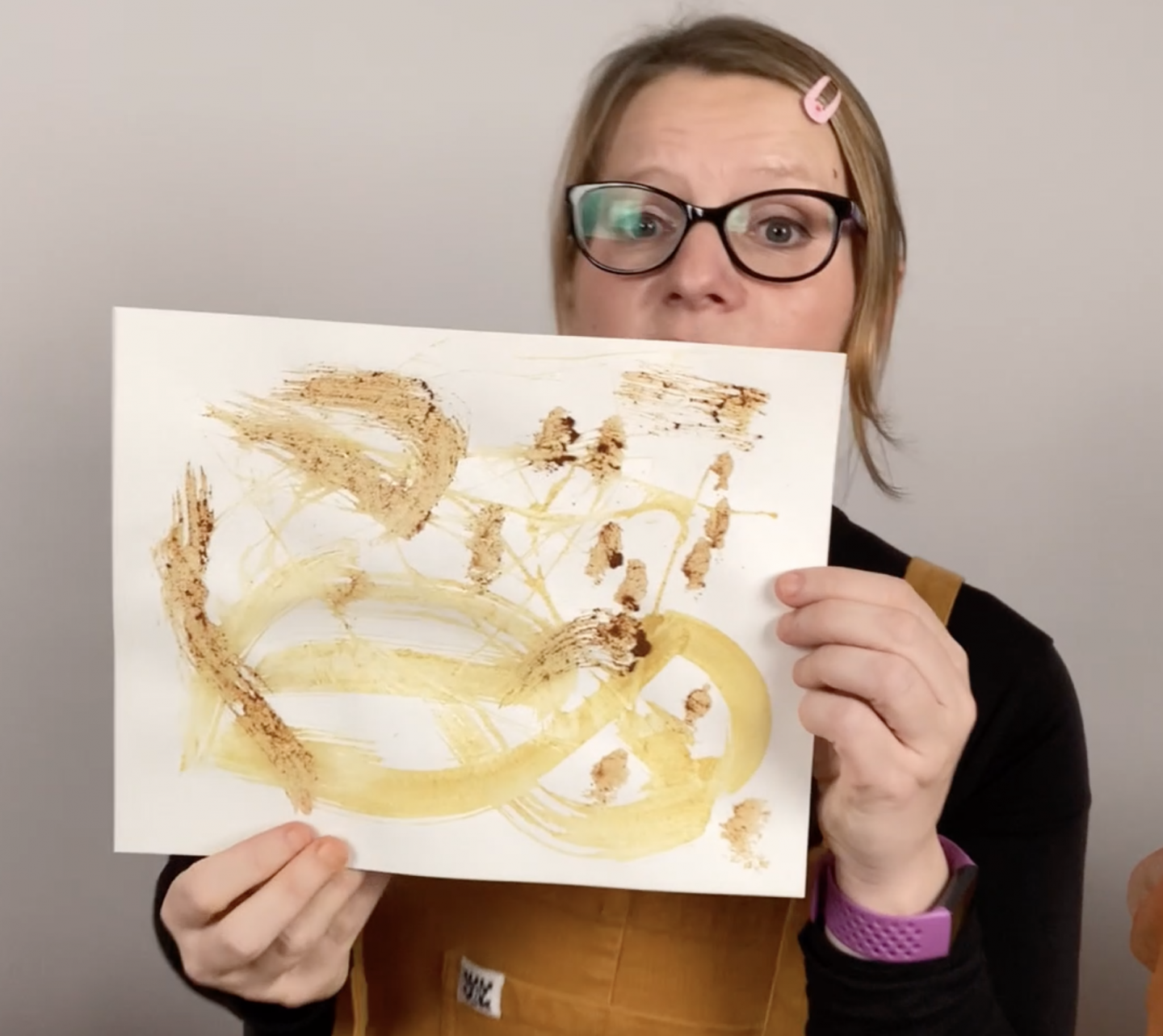 Someone holds up a piece of white paper. Swirls in yellow and brown have been created by painting with spices. 