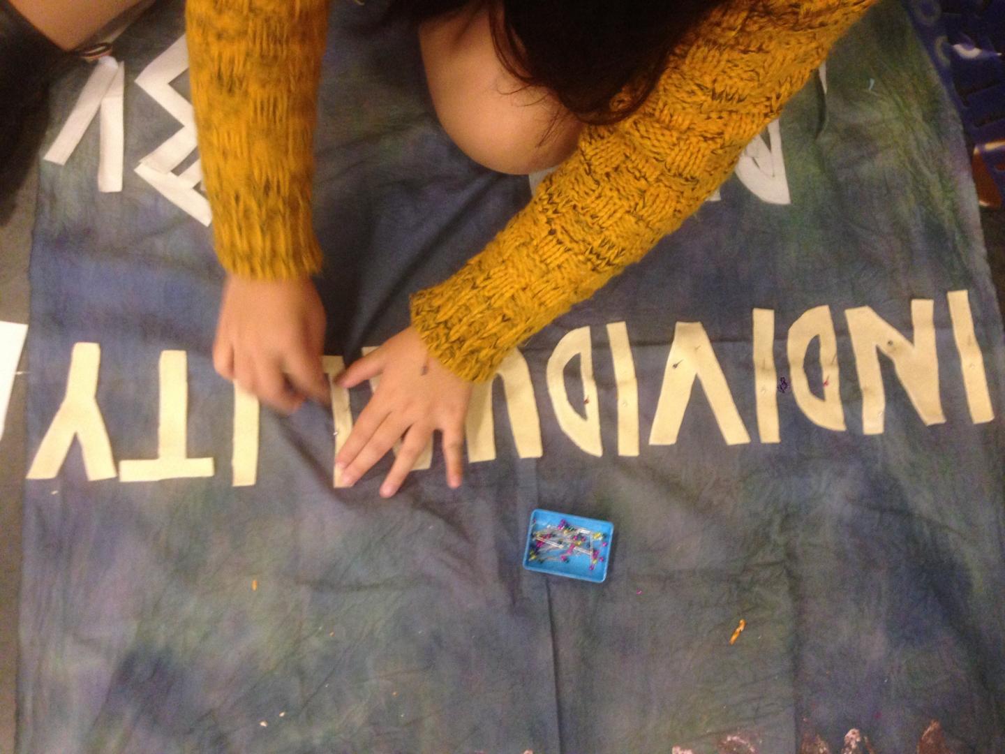 A young person sewing the words individuality onto a piece of fabric