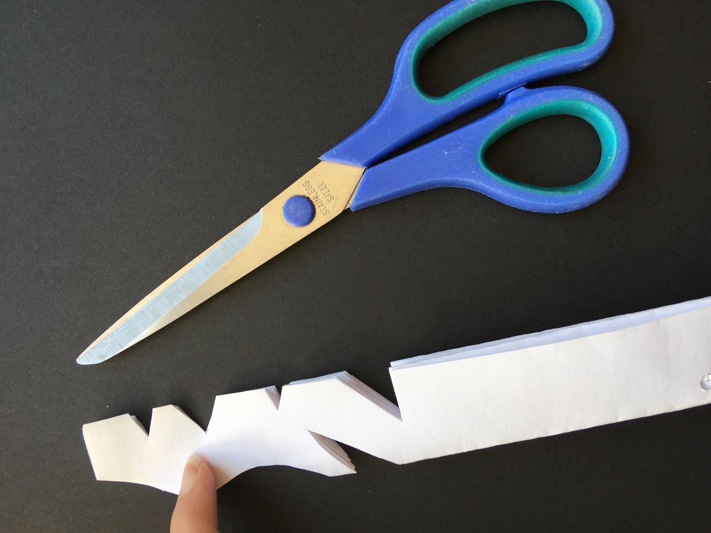 Shapes are cut into folded paper using scissors. 