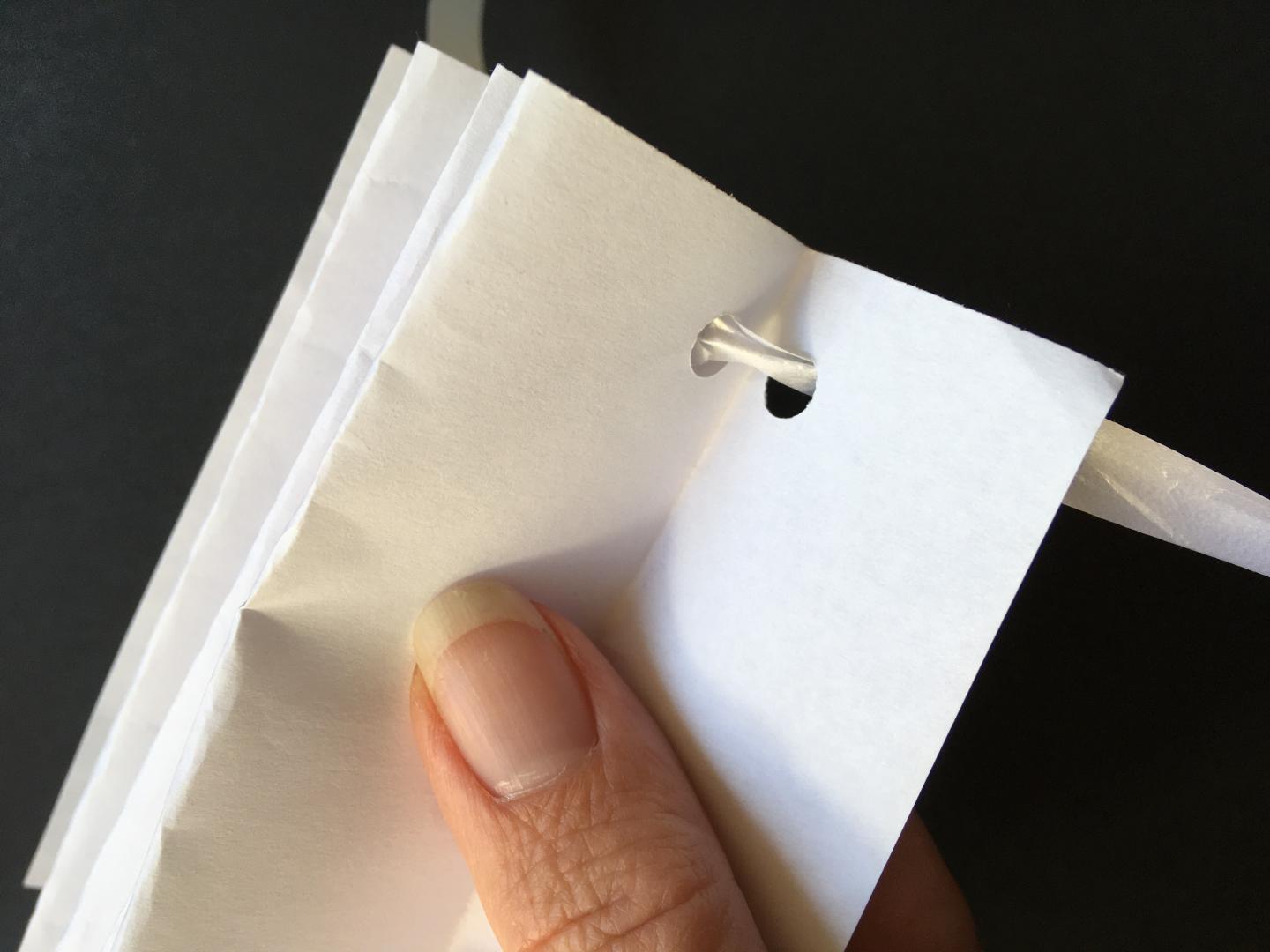 A piece of pleated paper with a hole at one end. String is threaded through the hole. 