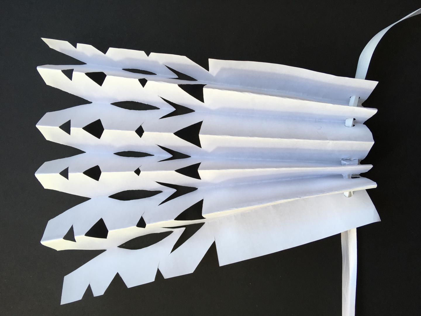 Pleated paper with cuts made to create a pattern. It is threaded onto string. 