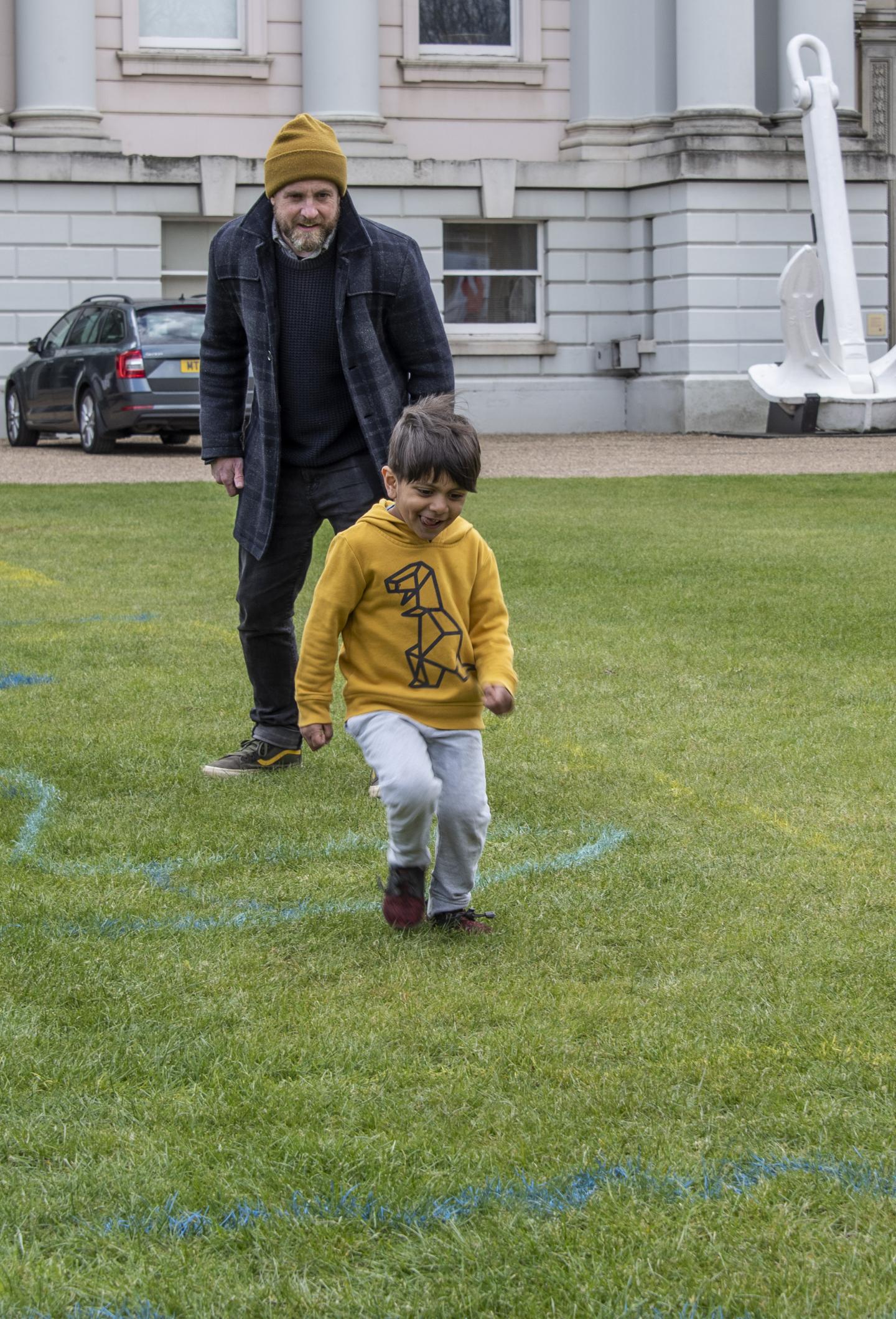 A child and adult are following chalked lines on the grass.