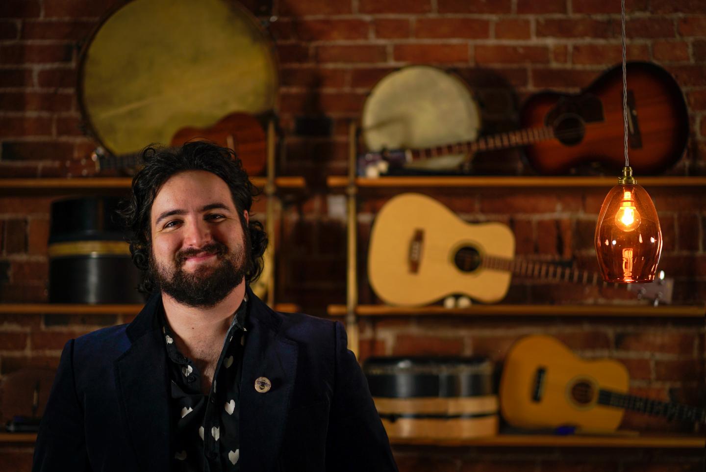 Image of a smiling man in a checked shirt standing in front of a guitar