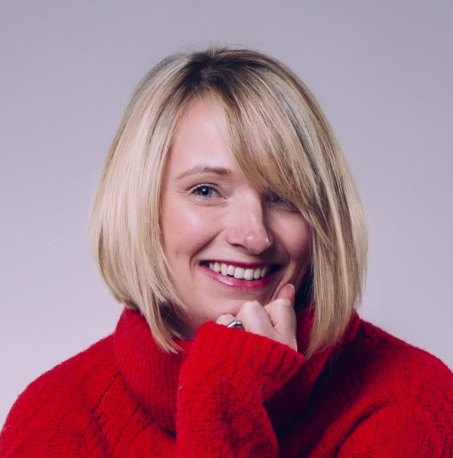 A photograph of Helen Dodd. Helen is a white woman with blonde, shoulder-length hair. She wears a red jumper.