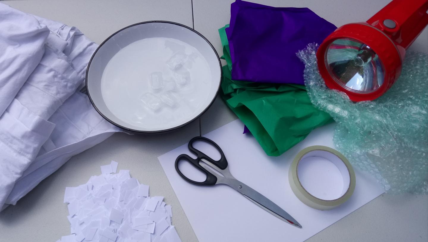 A photo of the materials needed. A bed sheet, bowl of water and ice, scissors, paper, torch, bubble wrap, coloured tissue paper, tape.