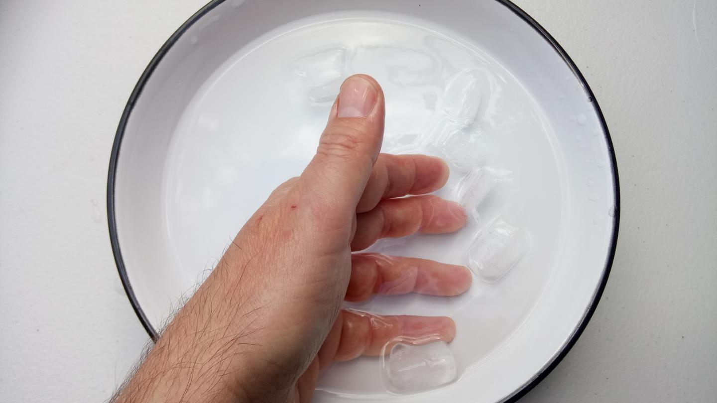 A bowl with water and ice in. Someone has their hand in the bowl.