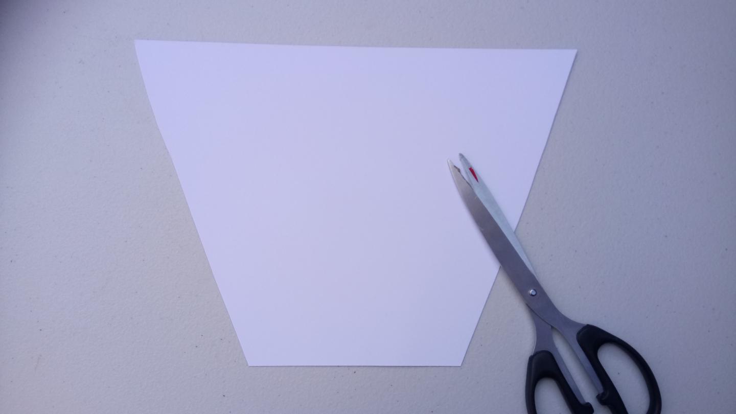 A piece of white paper cut into a trapezoid with a pair of scissors nearby.