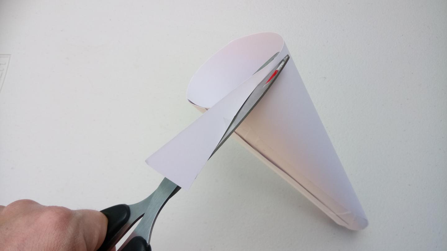 The end of a paper cone is being trimmed with scissors to create a flat edge.