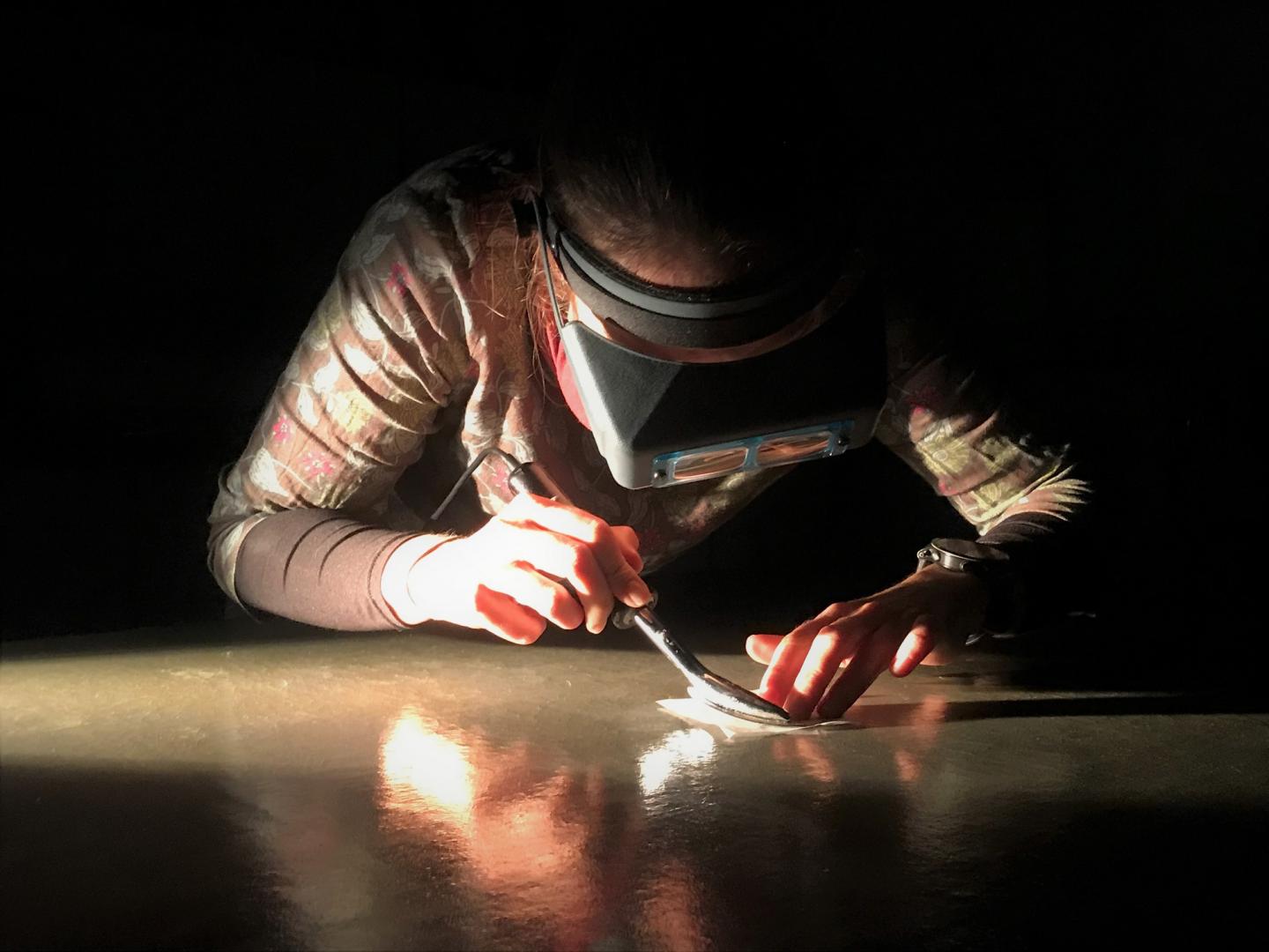 A conservator examines a painting in a darkened room