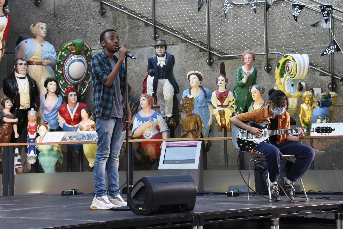 Two young performers on stage at Cutty Sark in front of the figure heads