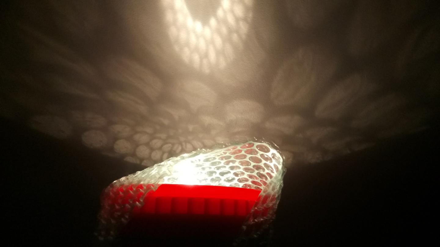 A torch shining through bubble wrap to create patterns on a white surface.