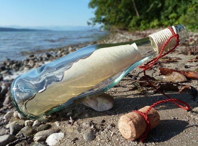 a clear bottle with a message inside, lying on a stony shoreline