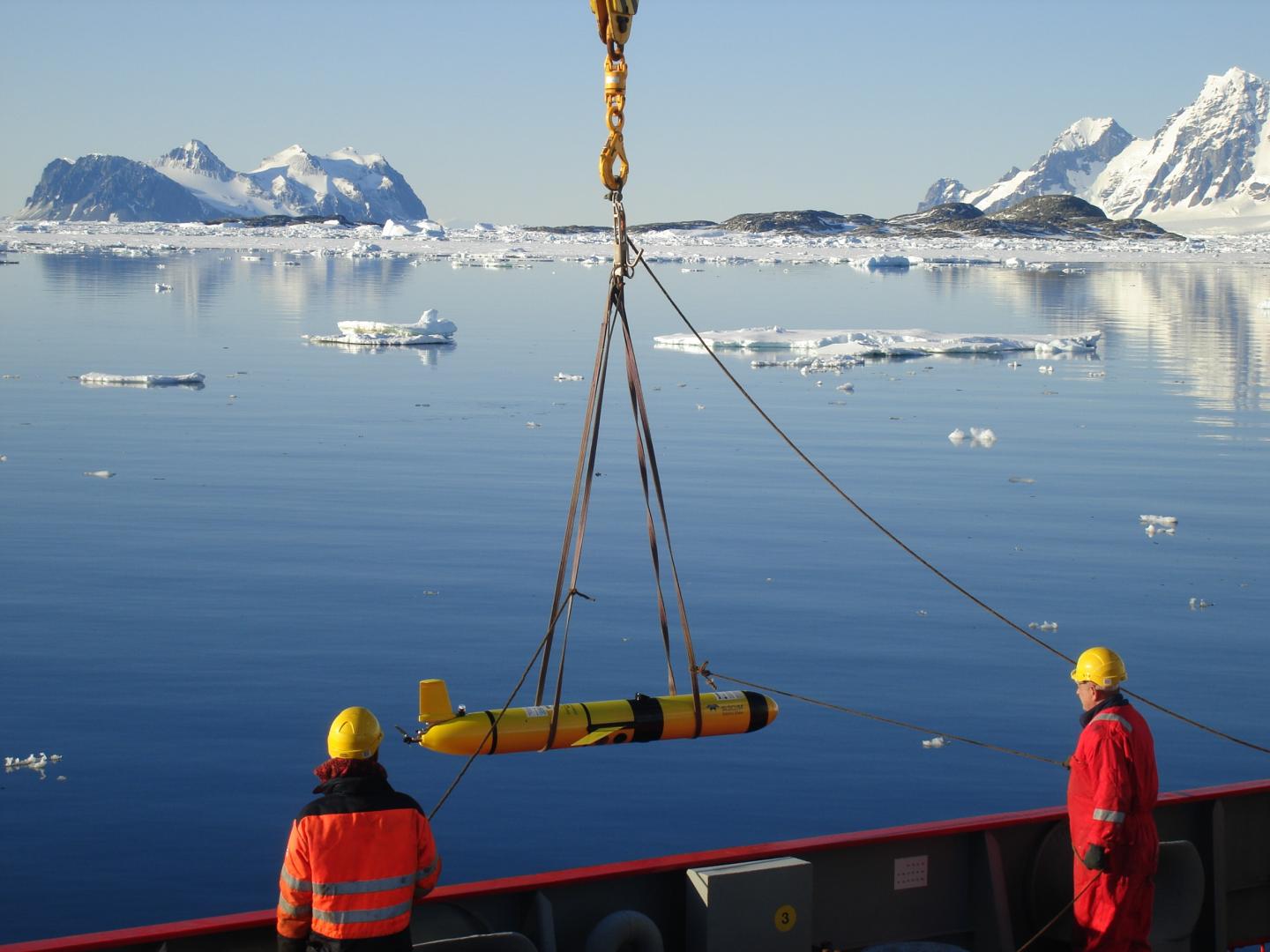 A team lower a polar robotic 'glider' into the water from the deck of a ship, with icebergs in the background