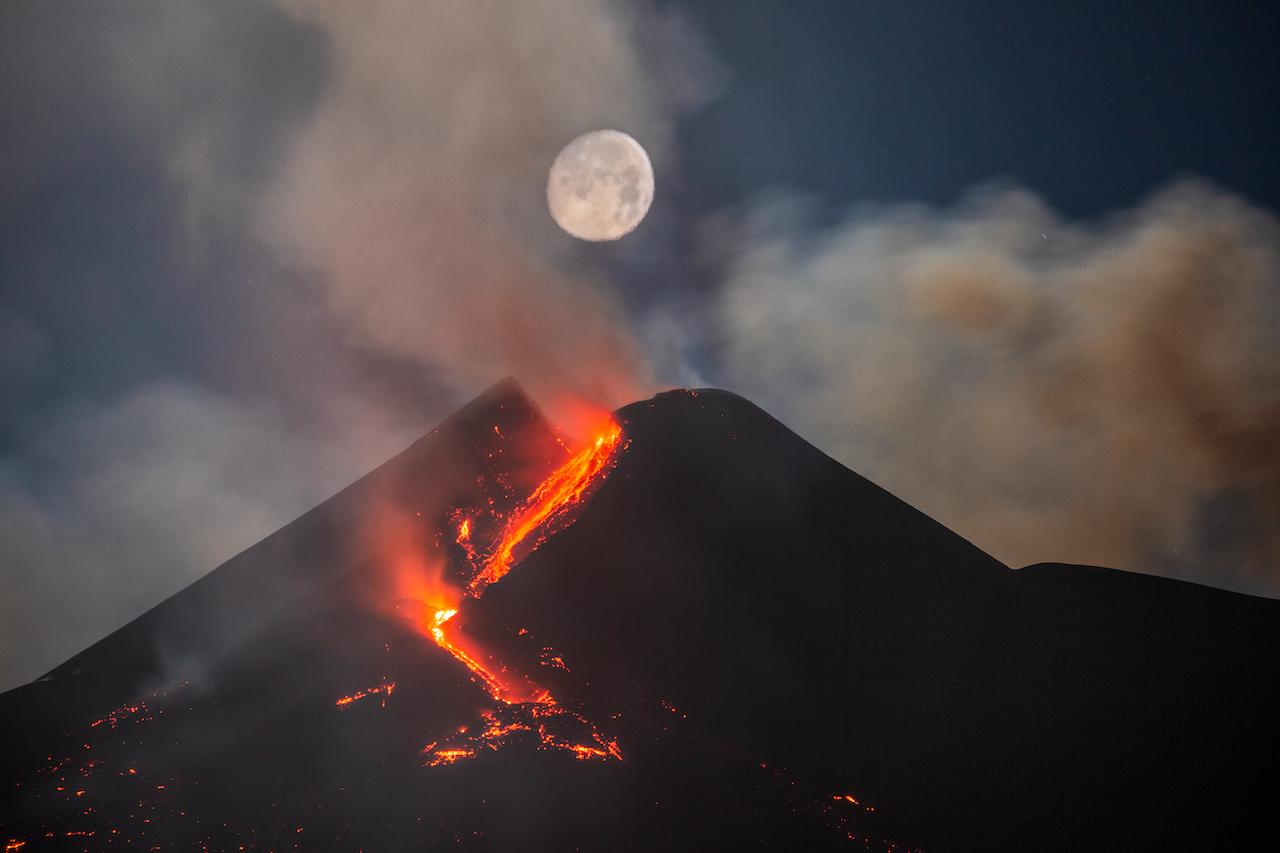 A full Moon rises over Mount Etna during an eruption