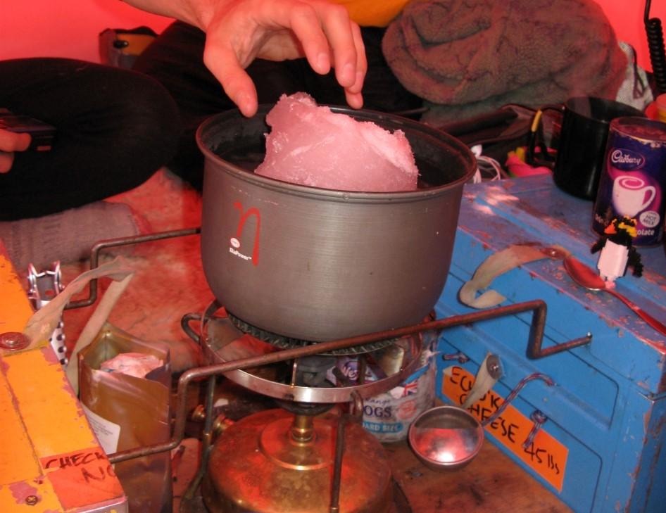 A block of ice in a pan on top of a stove, inside a tent during an Antarctic field expedition
