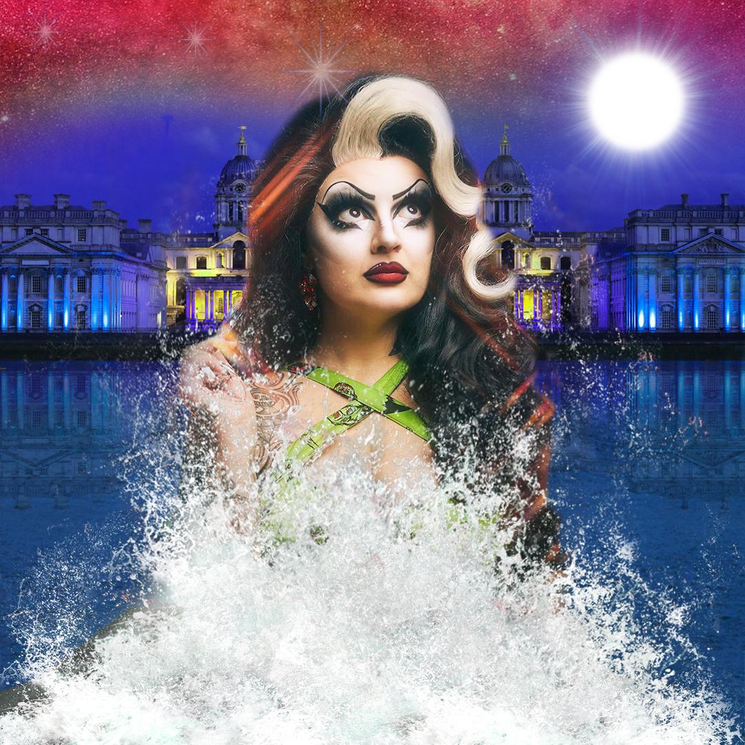 Mynxie wears a luscious long dark wig with a curled blond highlight, a full face of striking makeup and pensive look as they stand in the River Thames with the Queen's House behind them, waves crashing around them. 