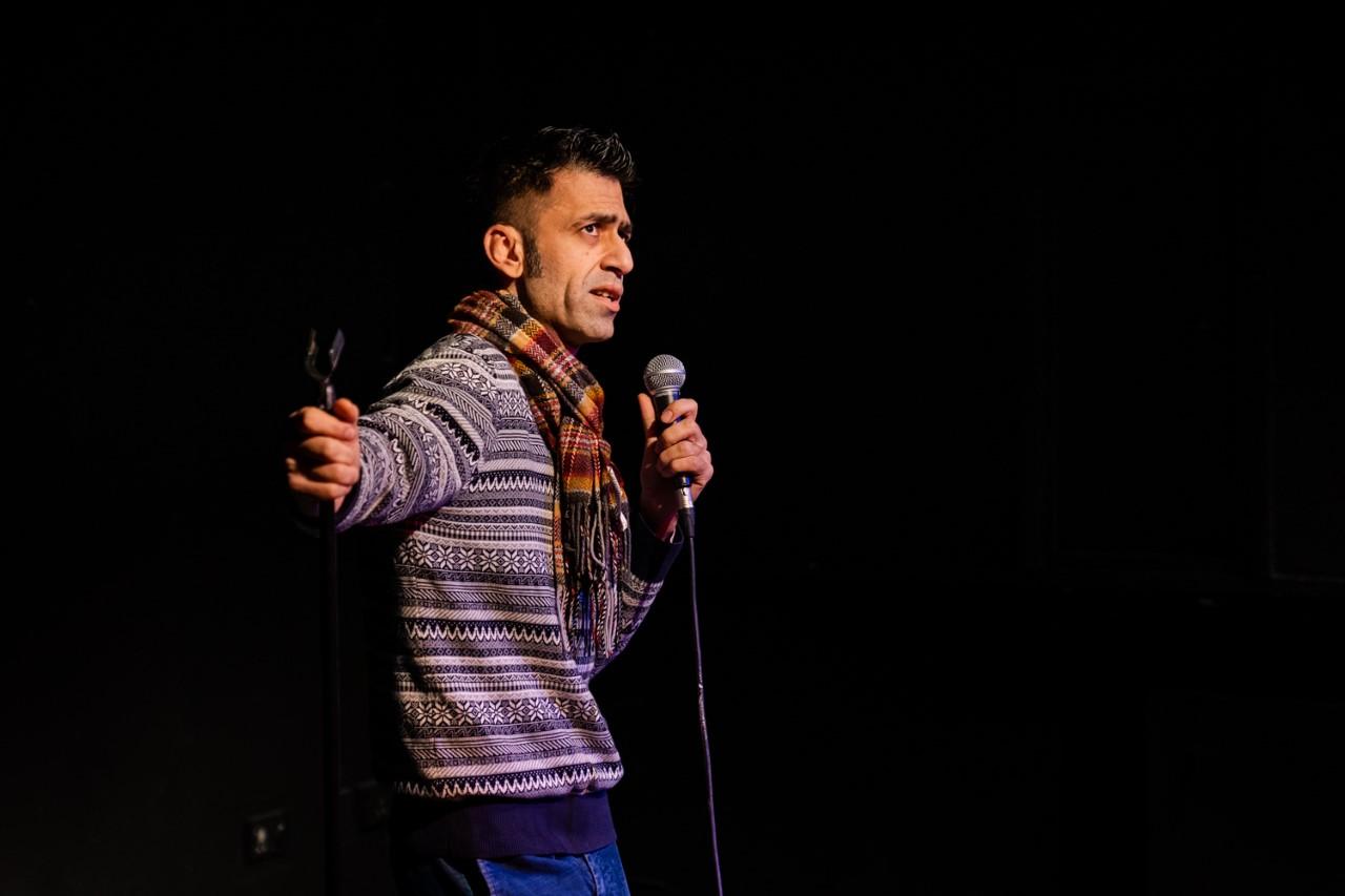 A man holding a mic and a mic stand wearing a scarf