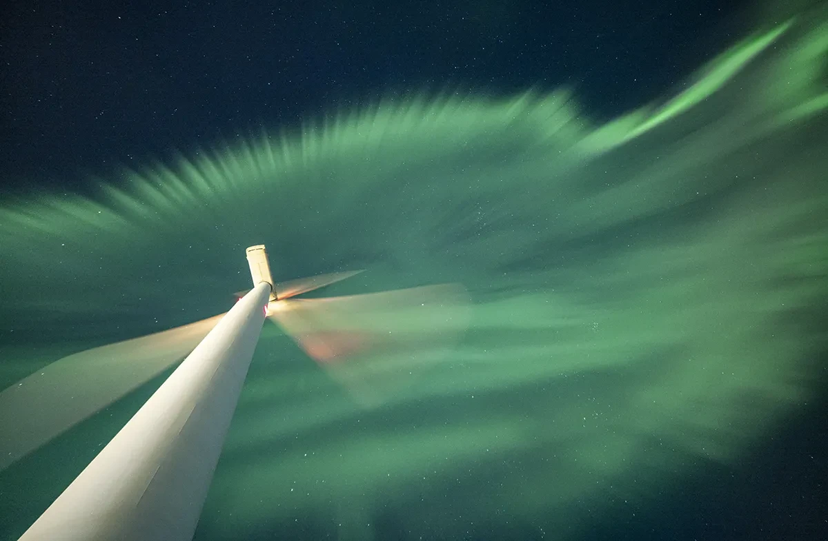 An astronomy photograph showing wind turbine at night, with green curtains of the aurora cascading overhead