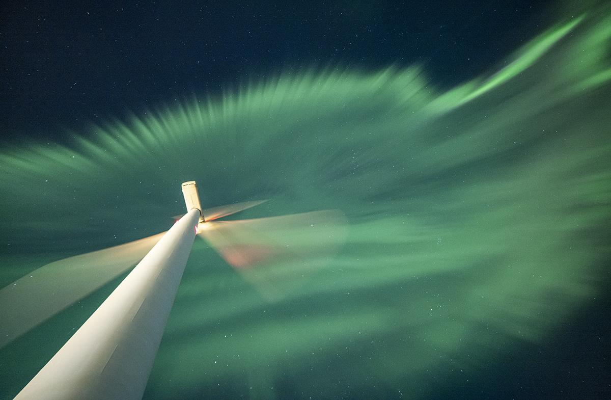 An astronomy photograph showing wind turbine at night, with green curtains of the aurora cascading overhead