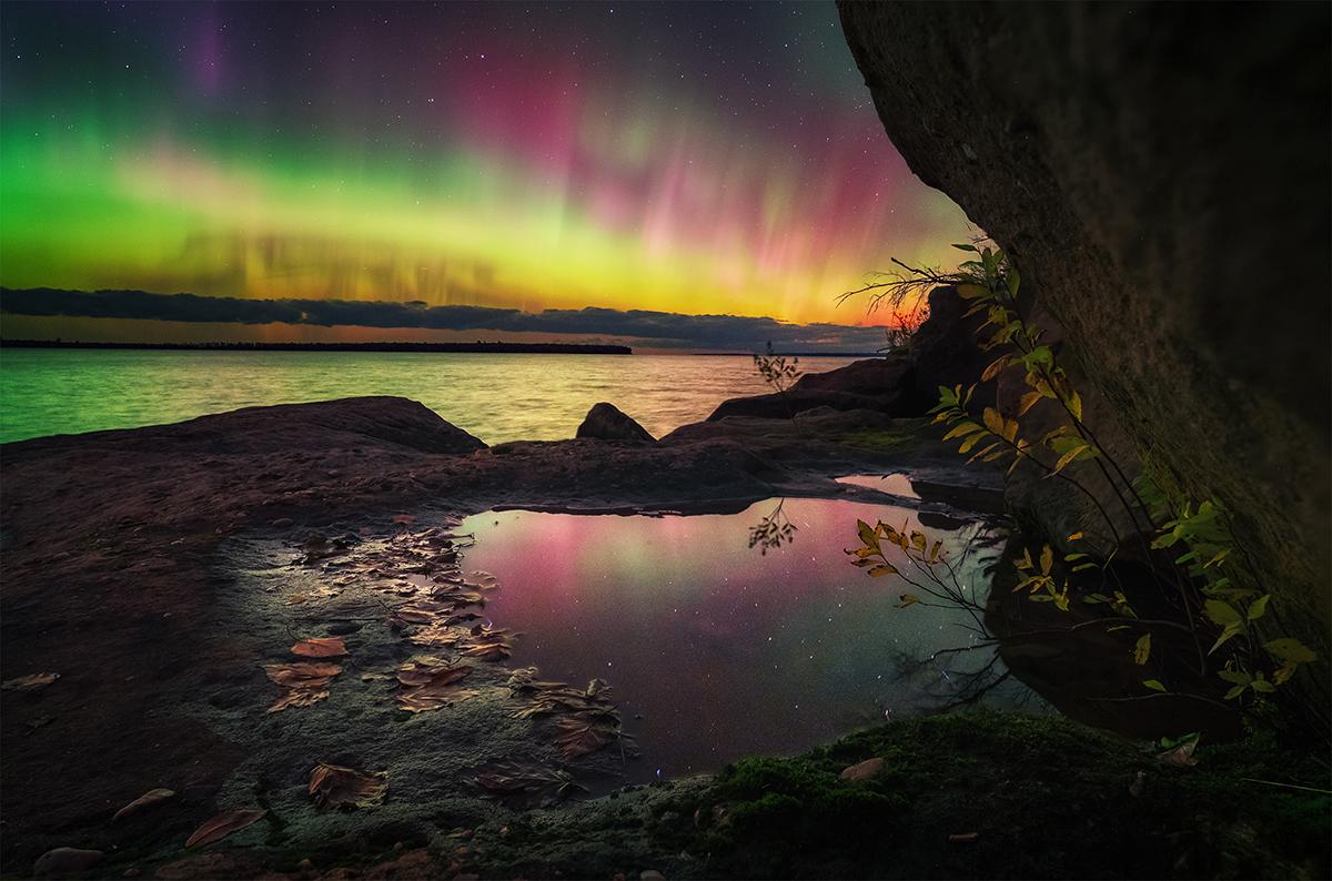 Image of body of water with green, purple and yellow aurorae in the sky