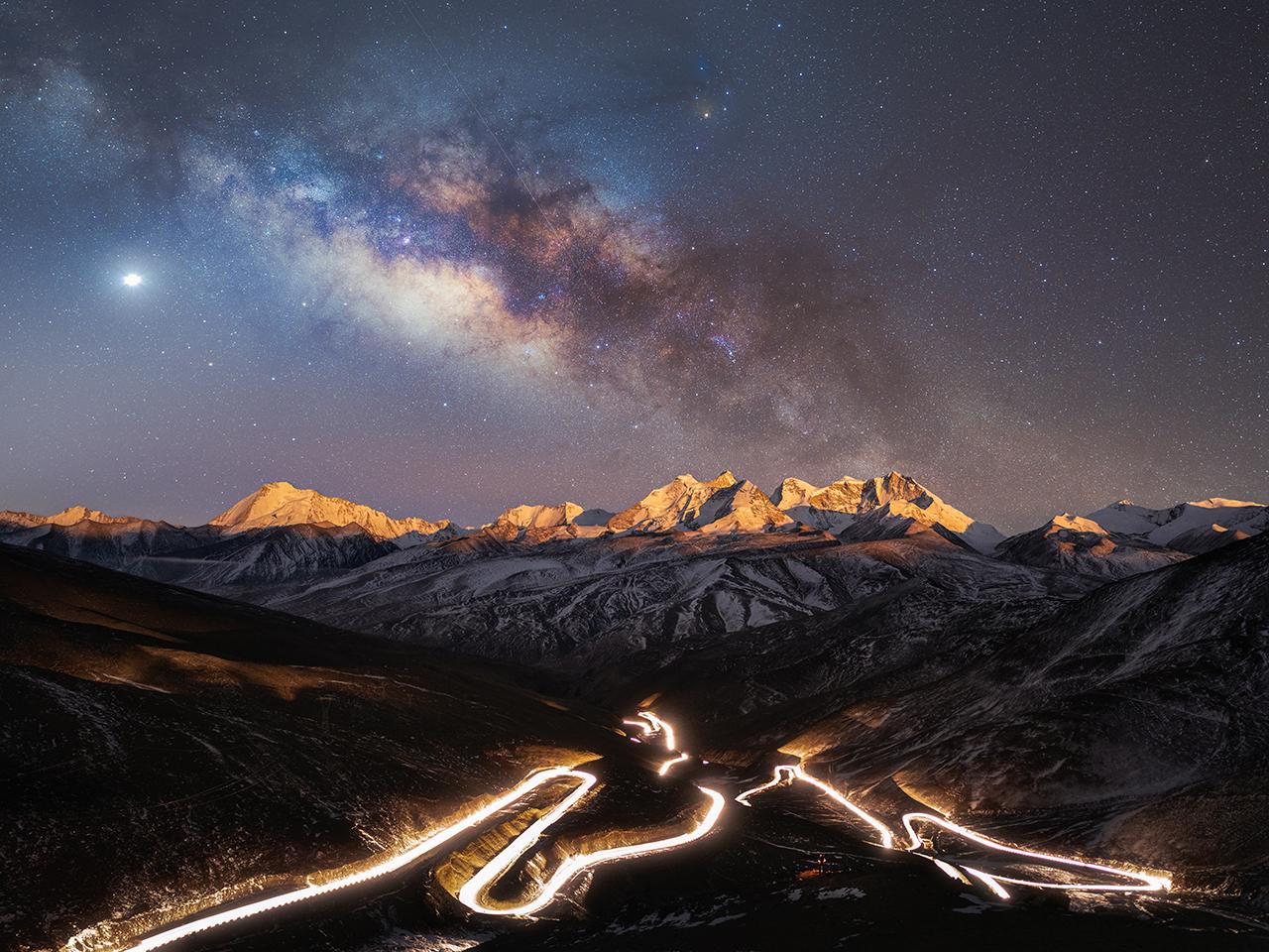 Long exposure of a long highway on a mountain with mountains and starry sky in the background