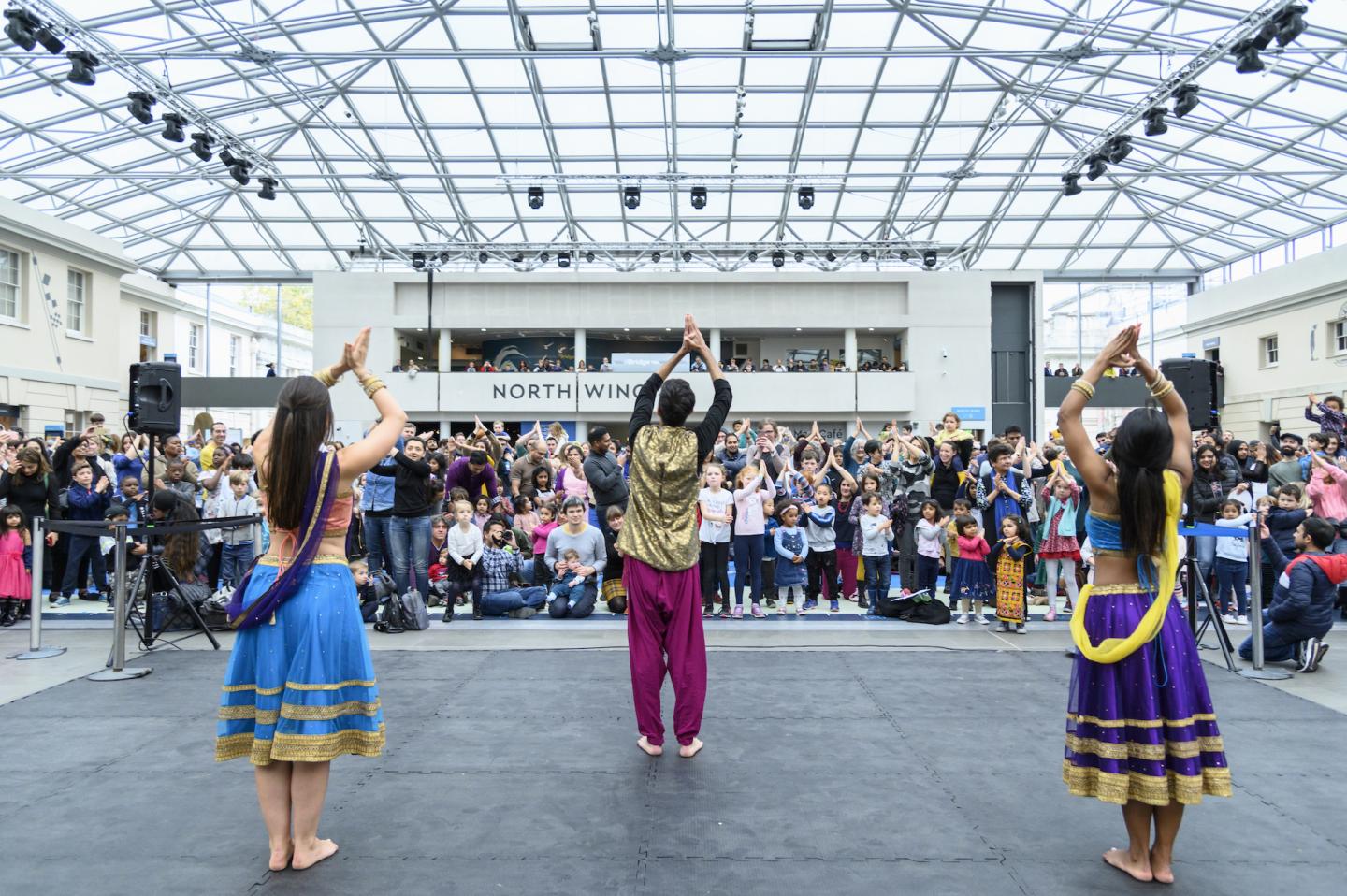Three dancers perform under the glass dome of the National Maritime Museum in front of a crowd as part of Diwali celebrations