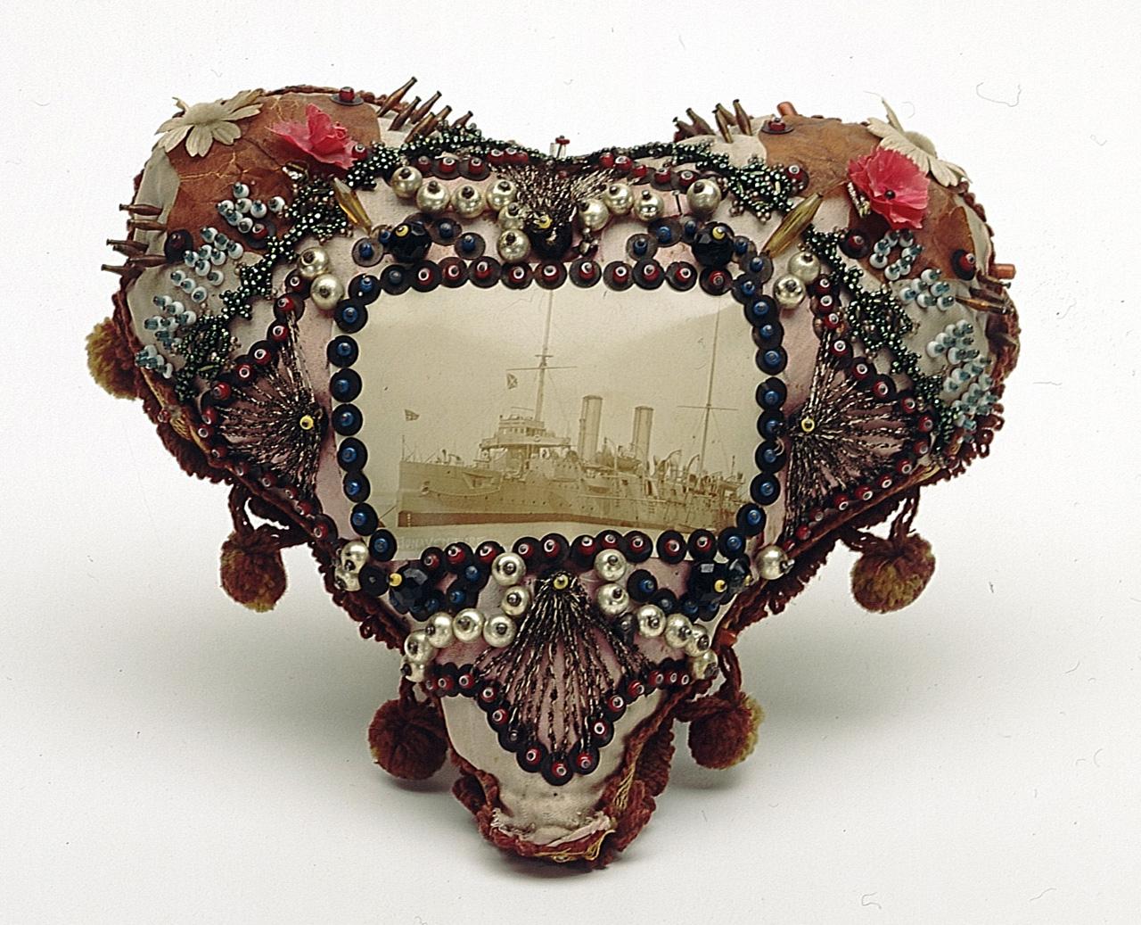 A padded heart-shaped cushion in pink and white silk with a photograph of HMS 'Bonaventure' is mounted in the centre