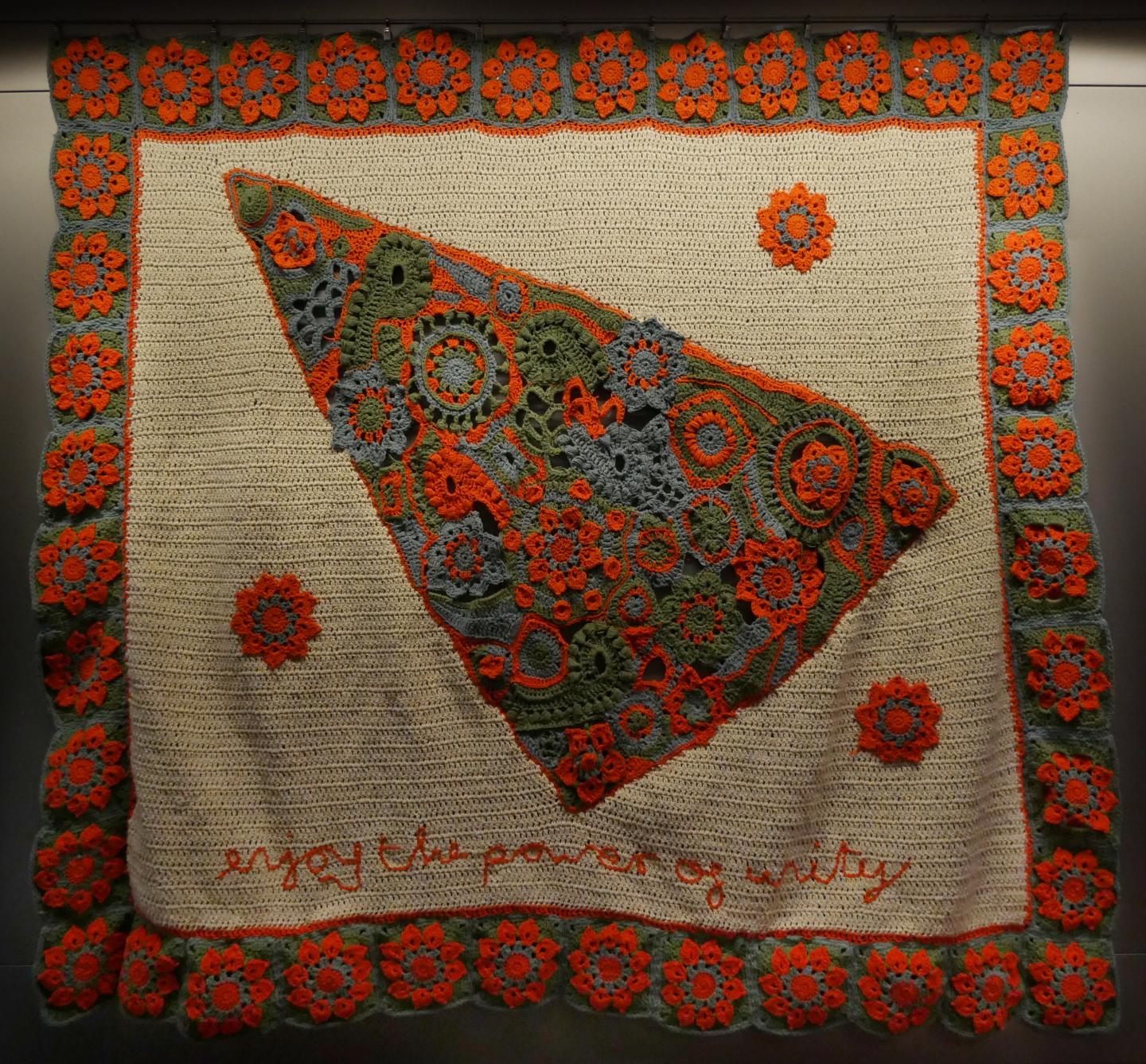 An orange, green and blue kanga with a colourful border and central triangle with the words 'enjoy the power of unity' at the bottom