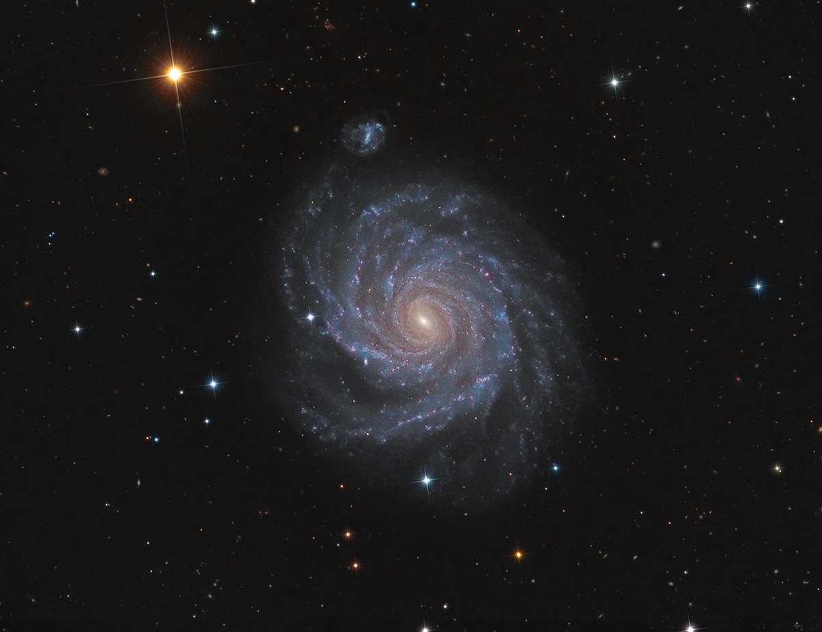 Close up of a galaxy with blue and purple clouds, with the background being a starry sky with one bright orange star standing out